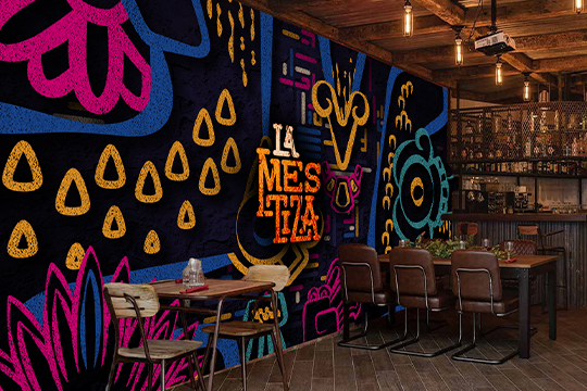 Aplicación de Branding en Interiorismo: Mural artístico con el sistema de grafismos 'El Alebrije' aplicado a gran escala sobre la pared de ladrillo del restaurante.