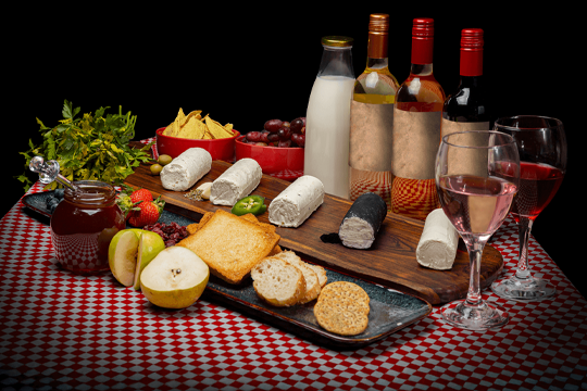 Producción Visual de Alta Gama: Bodegón fotográfico comercial y de producto para Quesos La Blanc sobre mantel de cuadros, con maridaje de vino, frutas y pan.